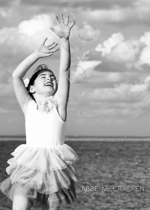 young girl joyfully reaches for bubbles while playing on the beach