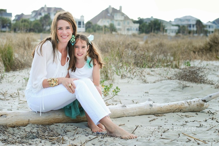 mother and daughter sitting on driftwood with toes in the sand
