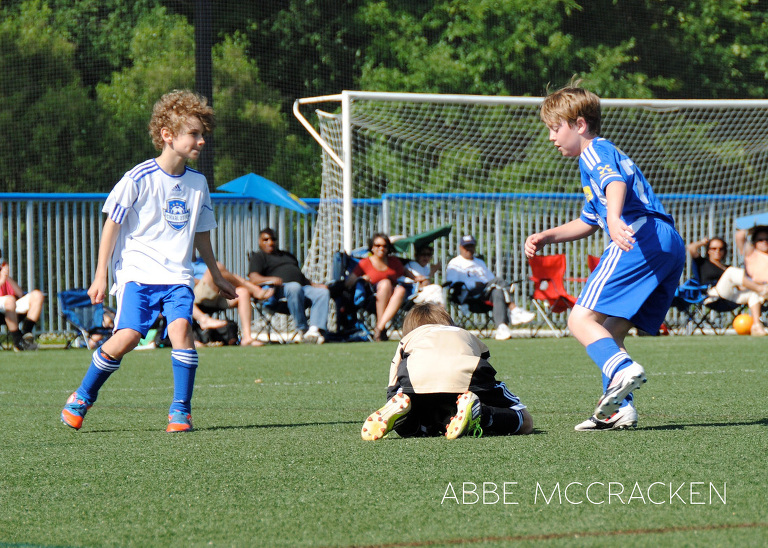 children's sports photography - soccer goalie covers the ball from opponents