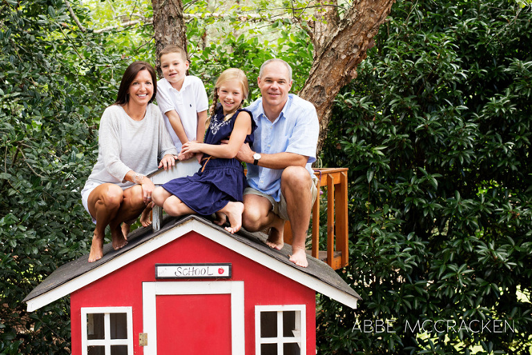 family of four sitting on top of playhouse in backyard