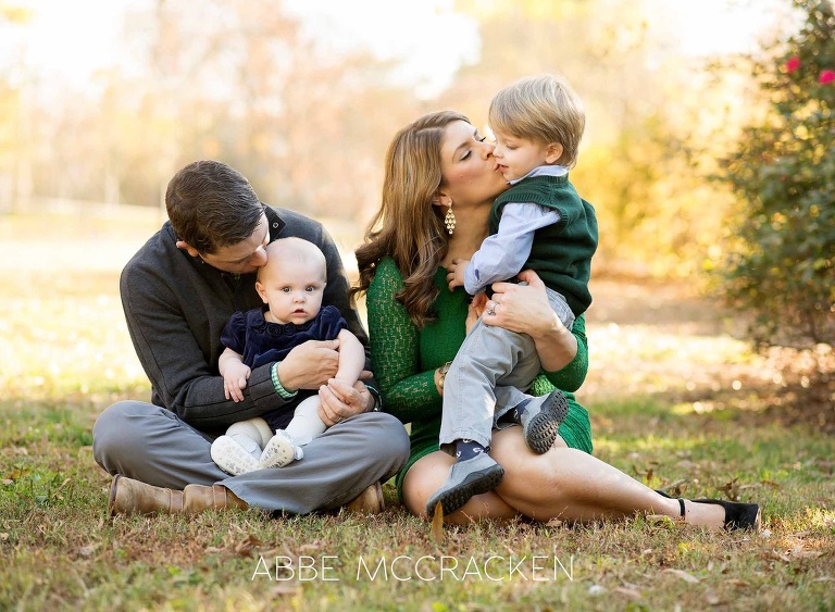 family of four, parents stealing kisses from young boy and baby sister