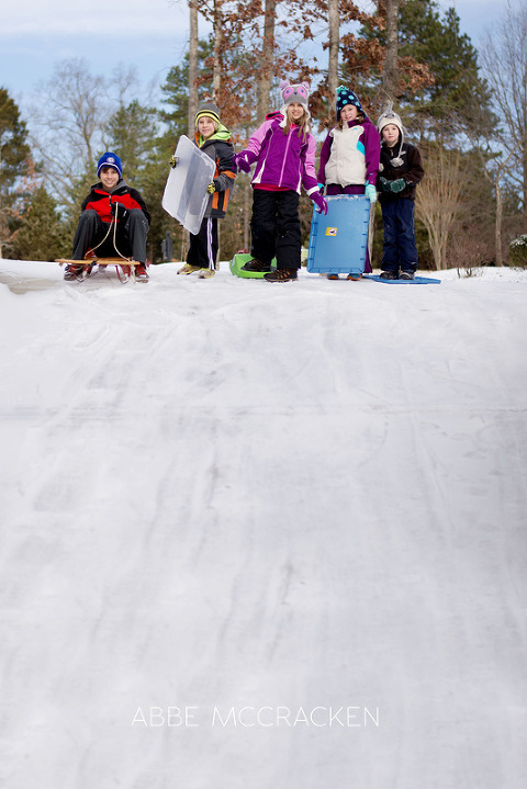 neighborhood children preparing to sled down driveway in snow