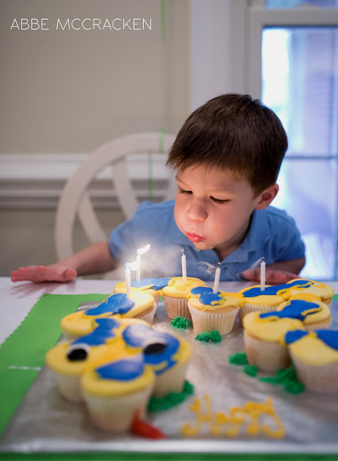 birthday boy blowing out candles on his snake themed cake of cupcakes