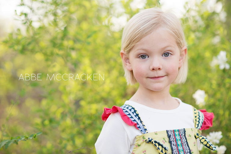 adorable little sister with rosy cheeks, spring flowers blooming behind her
