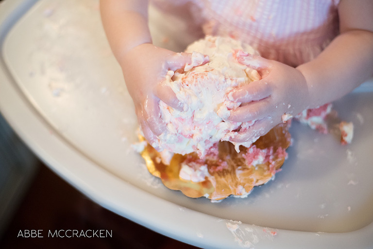 baby girl gets cake and icing all over her hands during first birthday smash cake