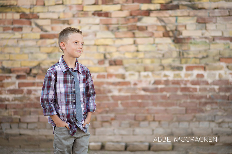 one cool kid - urban boy in plaid shirt and tie standing against a colorful brick wall