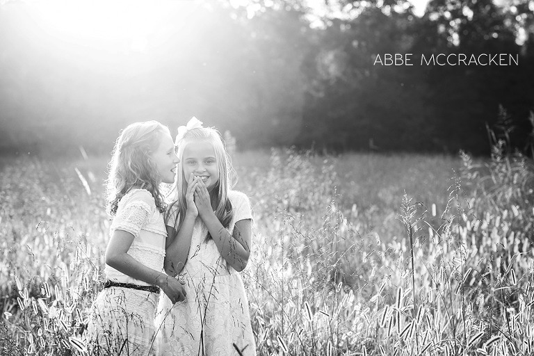 two children sharing whispers in backlit in a field