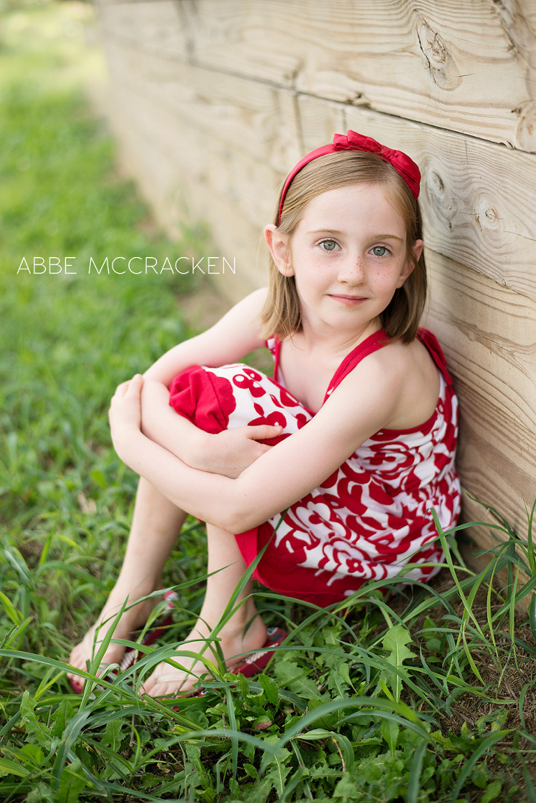 young girl in red and white dress sitting against a wood wall