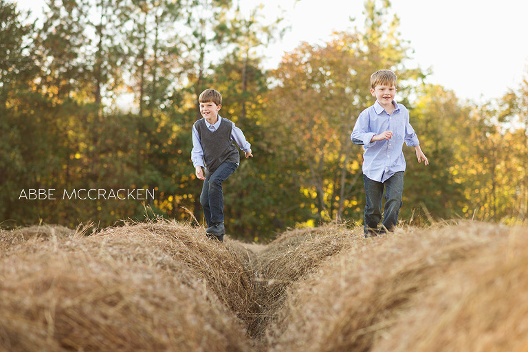 siblings running across the tops of hay bales at family farm