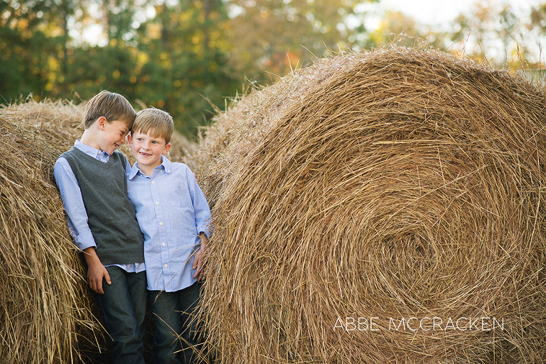 children standing in-between large hay bales telling secrets, family farm images