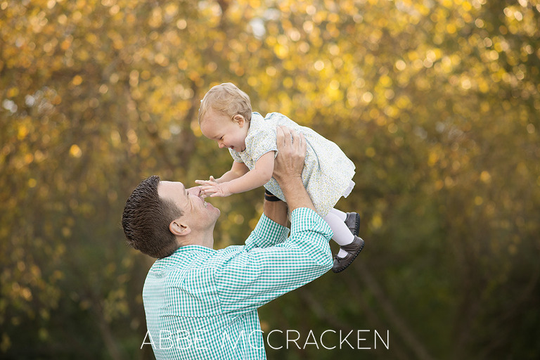 Daddy holding his one year old baby girl high in the air, sparkly bokeh behind them