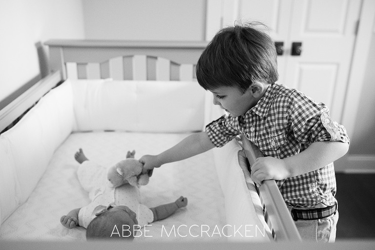 big brother leaning over crib to hand a toy to newborn baby brother