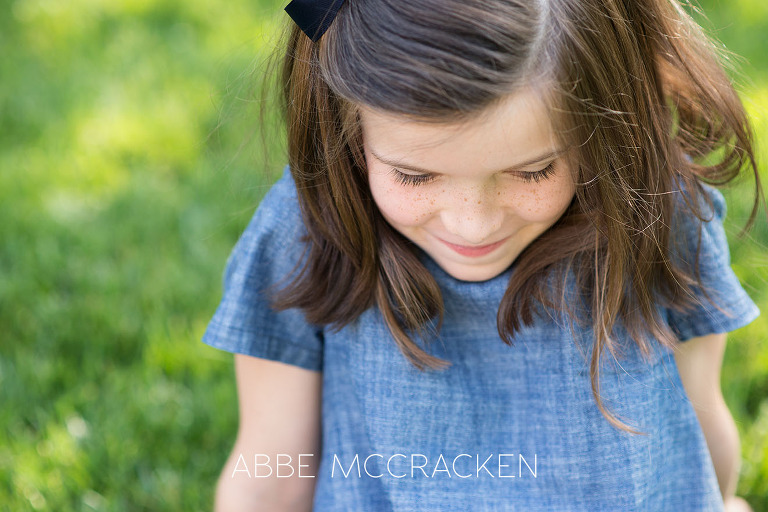 Close up of a young girl with freckles sitting in the grass on the grounds on Carmel Country Club