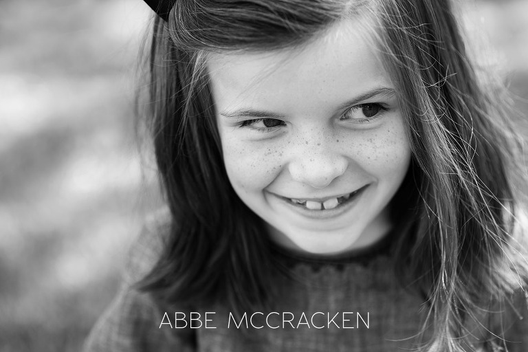 Black and white close up of a young girl with freckles sitting in the grass on the grounds on Carmel Country Club