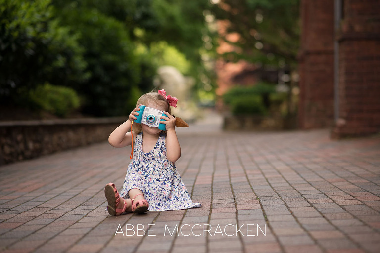 Young girl with toy camera. Image taken during a family photography session in Uptown Charlotte, NC