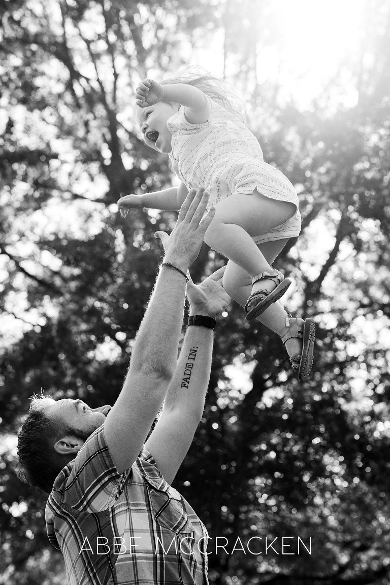 Family picture of a father tossing his two-year-old daughter into the air at Freedom Park