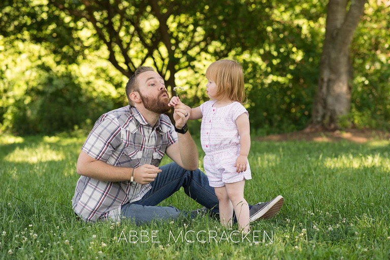 Picture of a father teaching is young daughter to blow dandelions.