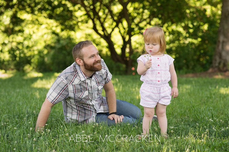 Picture of a father teaching is young daughter to blow dandelions.