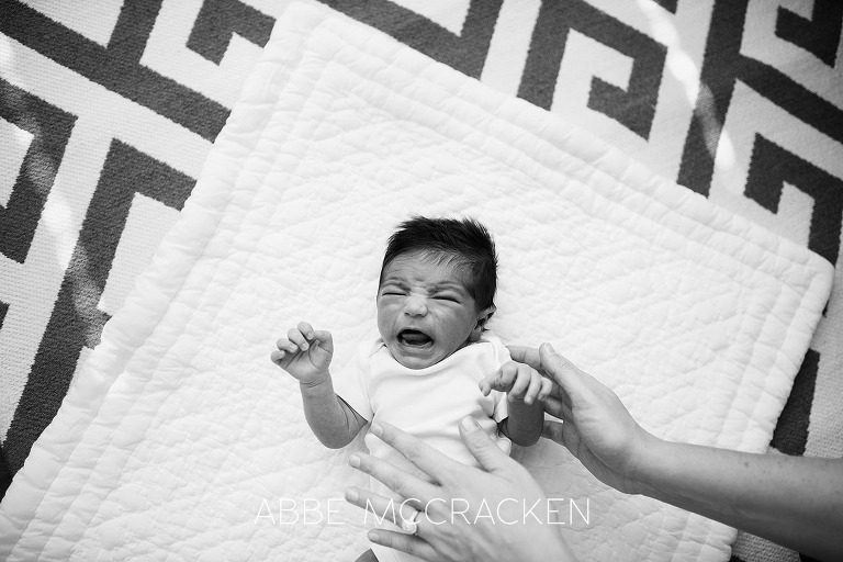 Black and white lifestyle portrait of a newborn baby boy fussing for mama's loving arms