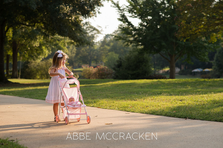 Three year old girl pushing her baby doll in a toy stroller along the paths of Charlotte's Freedom Park