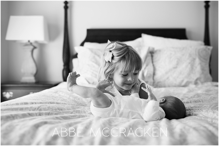 Newborn lifestyle photography session - candid moment of big sister and baby brother on bed