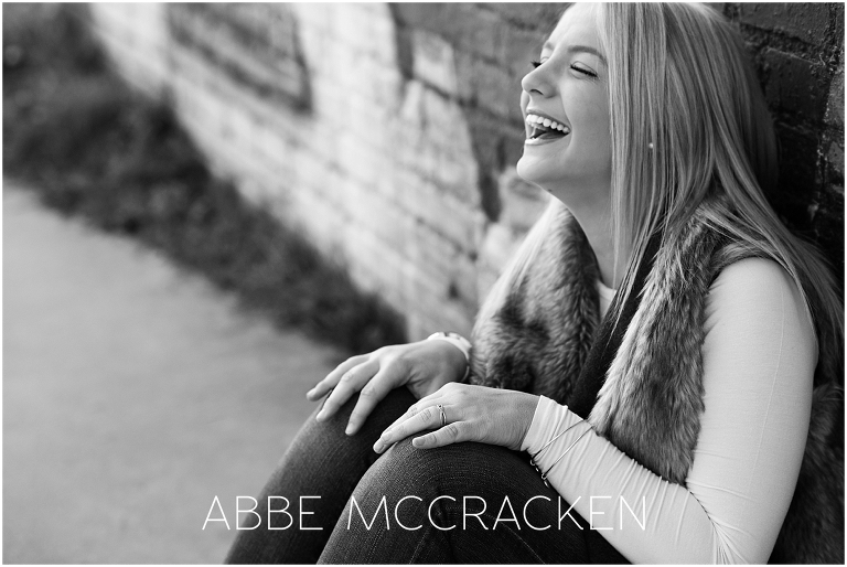 Black and white image of a high school senior laughing during her senior session in Charlotte's NoDa