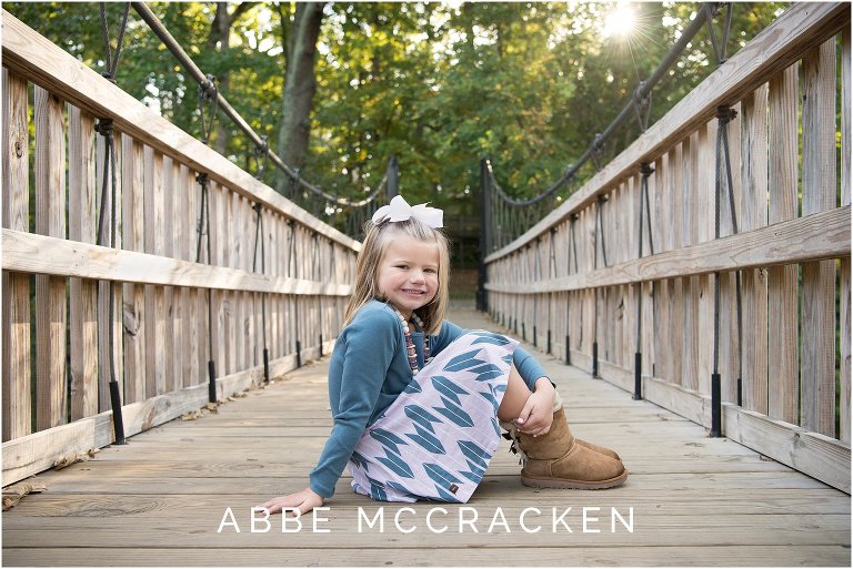 Portraits of a young girl sitting on a wooden bridge, sun flare in the sky