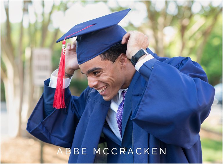 Candid image of handsome high school senior putting on cap and gown