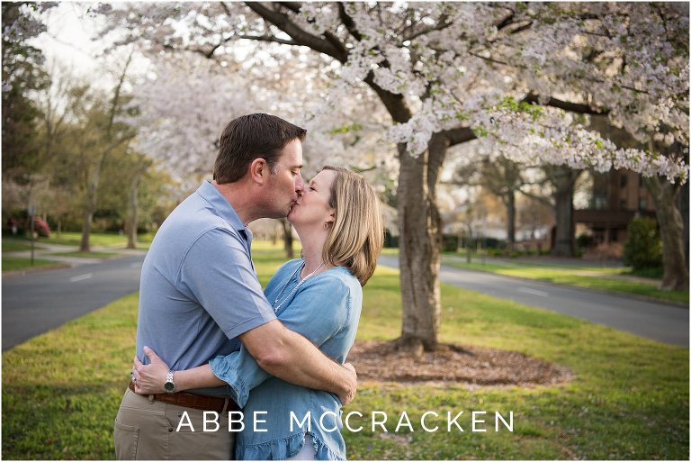 Parents kissing at the end of a family photography session and senior portraits for their son, gorgeous cherry blossoms above them