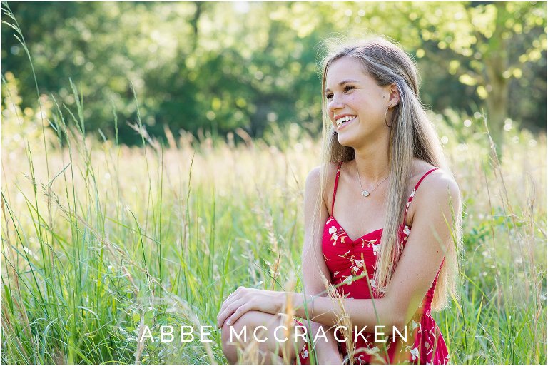 High school senior laughing at someone off camera while sitting amongst the tall grasses of a wheat field south of Charlotte, NC