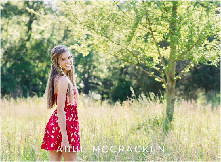 High school senior in a red romper standing in tall grasses, wheat field