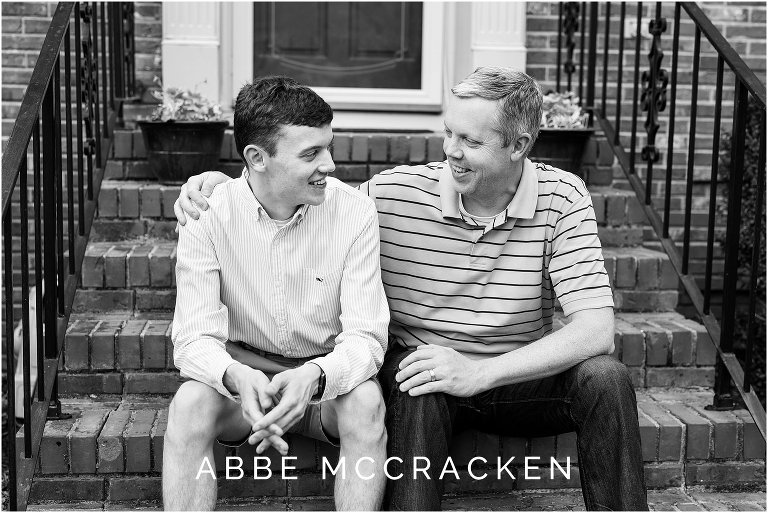 Black and white image of a father and son sitting on their front porch steps, high school senior portraits at home