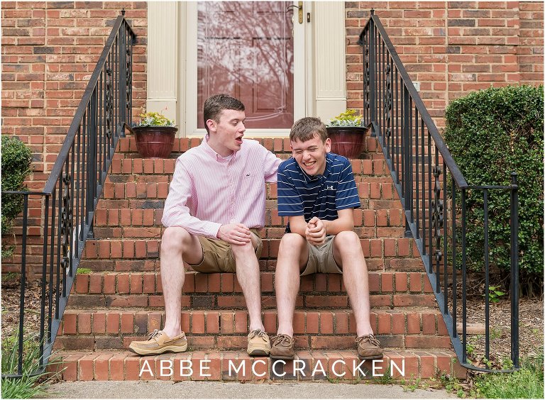 Candid senior portrait with a sibling - two boys laughing at each other on the front porch steps of their home