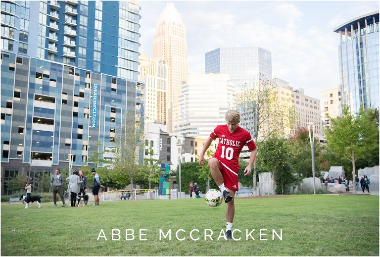 Athletic senior portrait of a boy wearing his Charlotte Catholic soccer uniform and showcasing moves in Romare Bearden Park