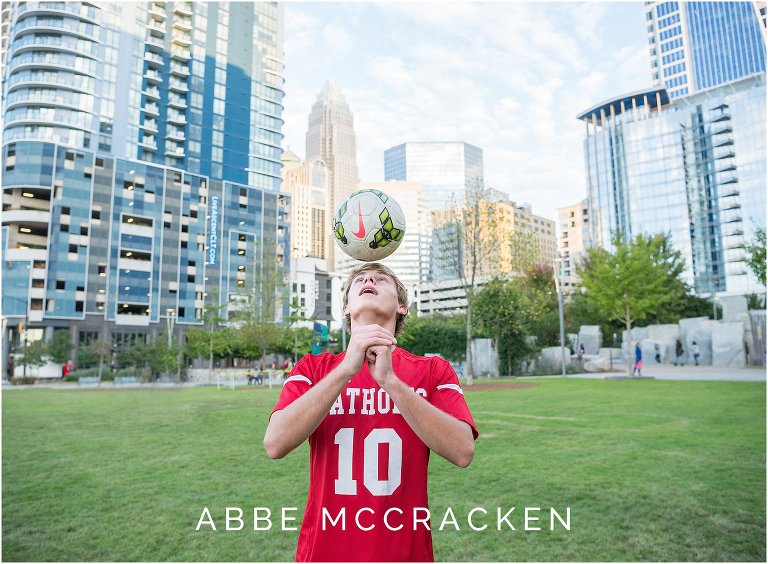 Athletic senior portraits of a boy wearing his Charlotte Catholic soccer uniform and showcasing moves in Romare Bearden Park