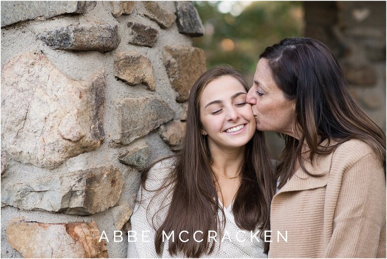 mother kissing high school senior daughter on the cheek