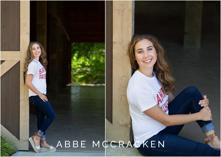 Girl standing and sitting against a barn for portraits in her college t-shirt, jeans and platform sandals