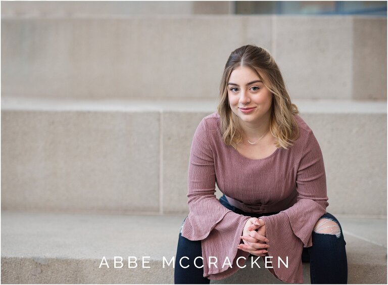 senior girl leaning forward on knees smirking at the photographer