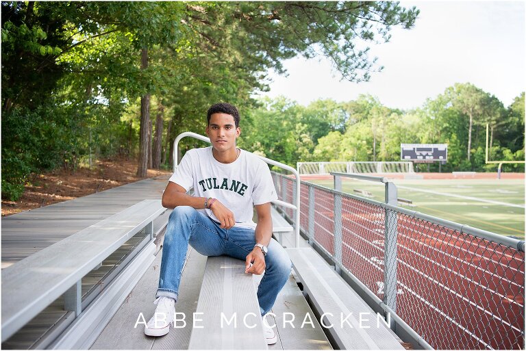Senior portrait sitting on the bleachers with a track in the background