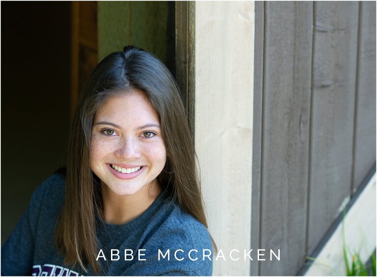 Senior portrait sitting beside barn door