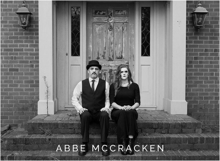 Halloween portrait of a mother and father sitting on steps of an abandoned home