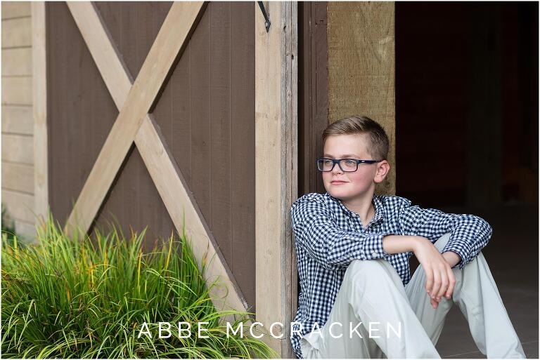 Boy in glasses sitting against a barn door