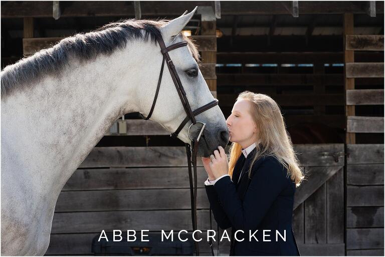 Equestrian champion kissing her horse, both are outlined in rim light coming from slightly above the stables
