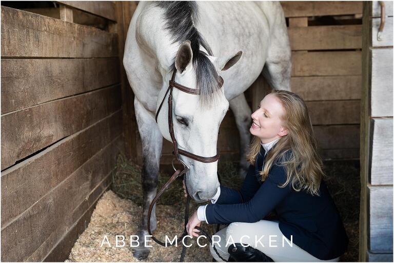 Senior picture of a blond girl and her white horse in the stables at Blowing Rock Equestrian Park