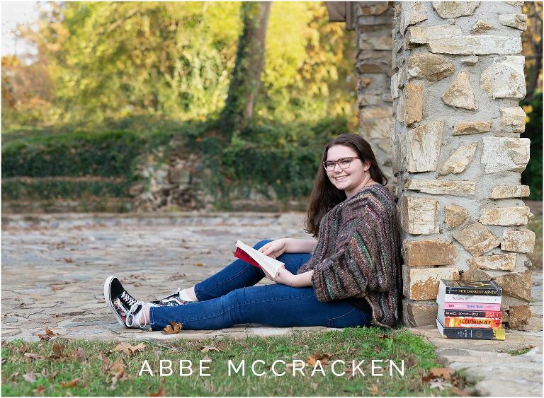 Fall senior photo of girl sitting against a stone column with her favorite books beside her