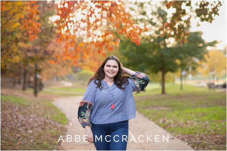 Senior portrait of a girl in Charlotte's Independence Park, gorgeous orange fall leaves above her