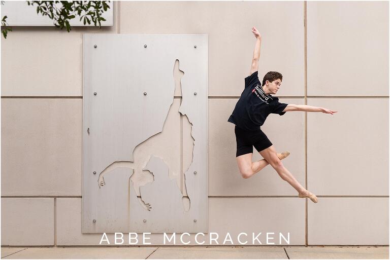 Senior boy mid air in ballet jump, composed next to art on the exterior of the Charlotte Ballet building