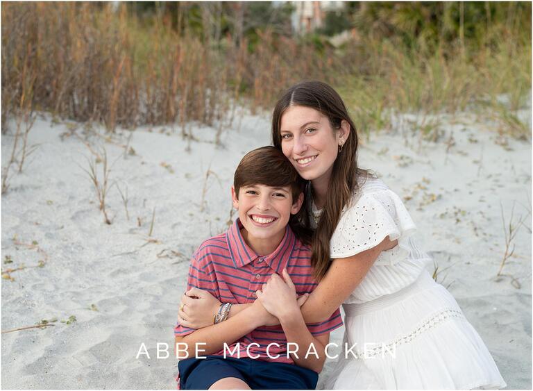 Picture of a high school senior sitting on the beach with her younger brother