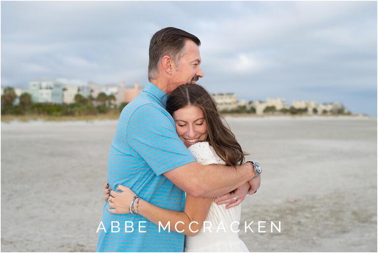 Father and daughter hugging on the beach, Wild Dunes Resort in the background