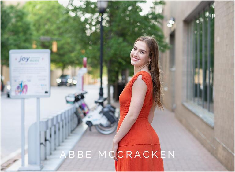 Girl in an orange dress standing on a sidewalk in Uptown Charlotte